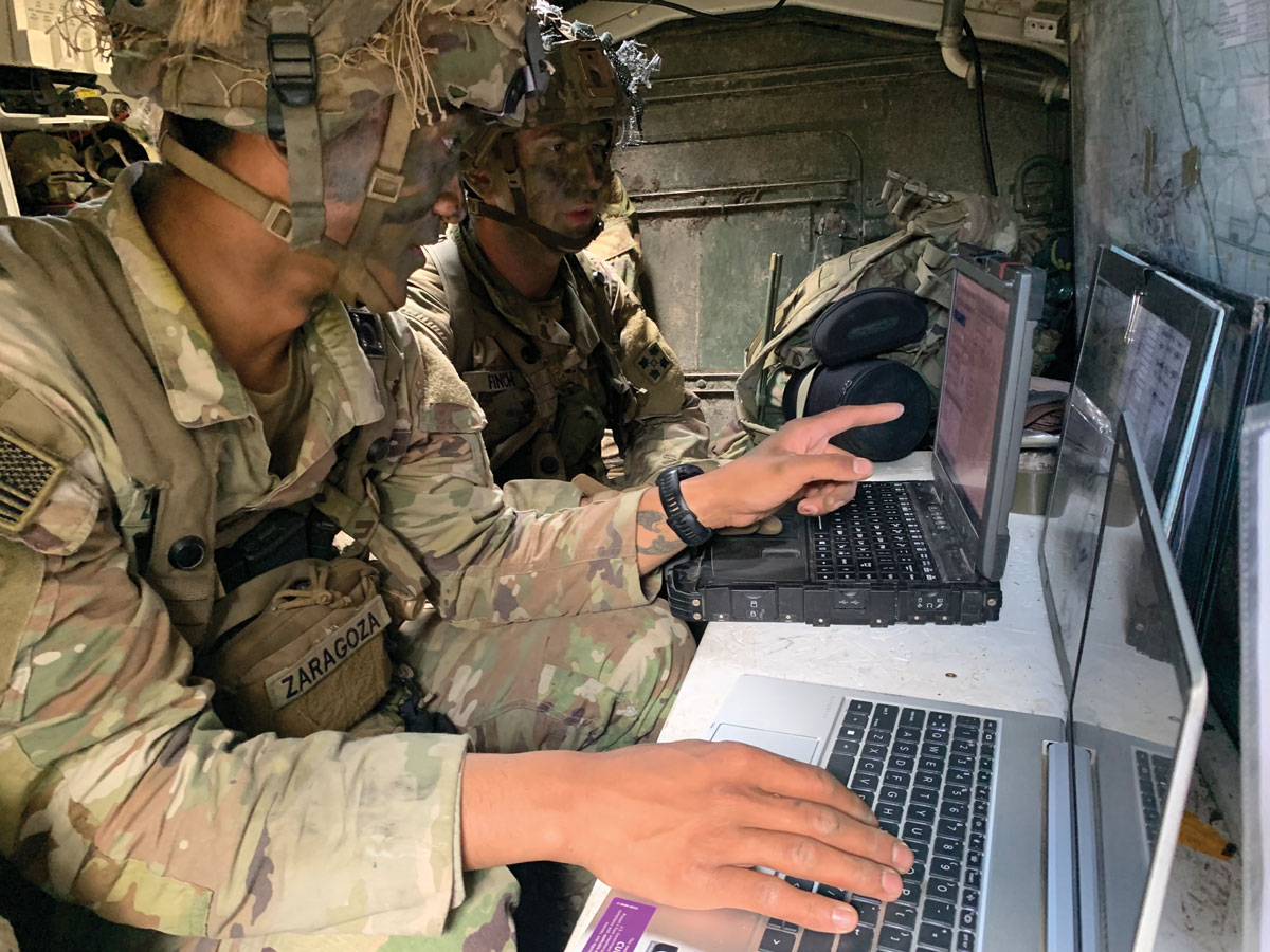 Two service members using data tools inside a Stryker tactical command post during a combat training rotation.